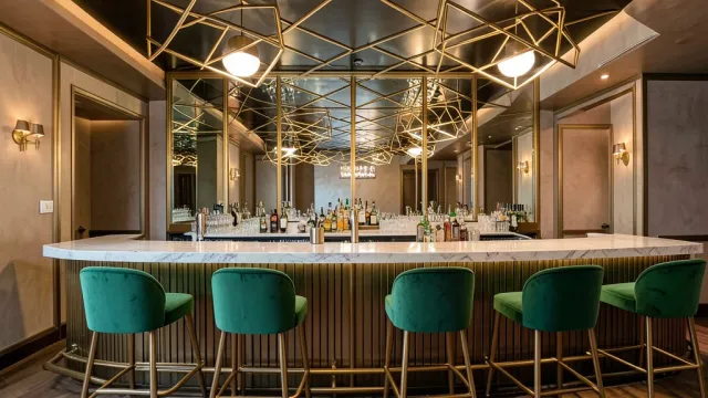 Elegant art deco cocktail bar with mirrored back wall, brass rails, emerald velvet stools, and geometric ceiling lights