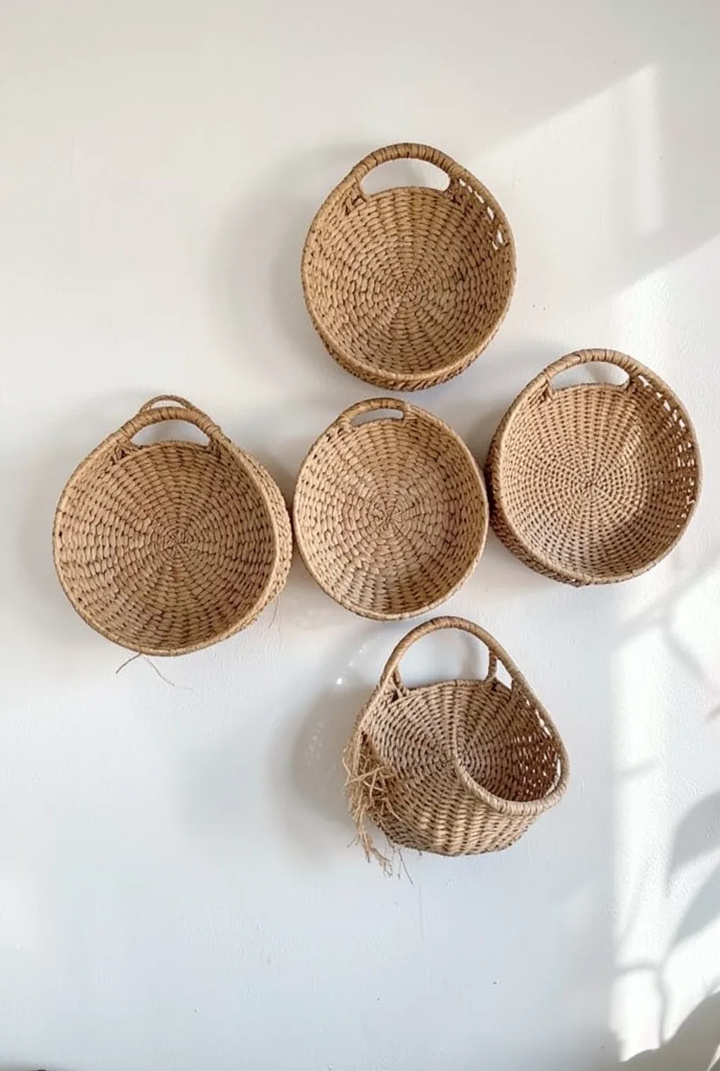 Three woven seagrass baskets in natural tones arranged on a white wall with soft shadows