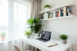 Bright modern home office with white desk, laptop, fiddle leaf fig, shelves, and large window