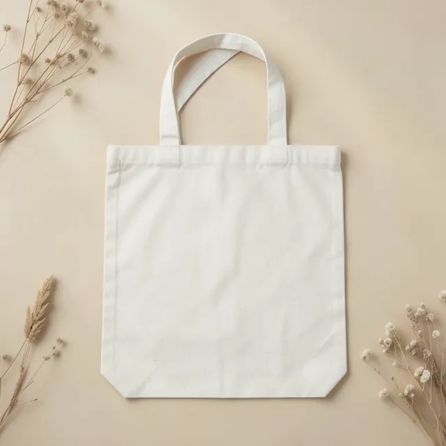 Top-down mockup of a plain blank natural canvas tote bag on a neutral surface with minimal props