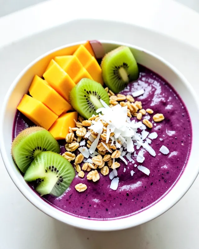Deep purple acai bowl topped with mango, kiwi, passion fruit, coconut flakes, and granola