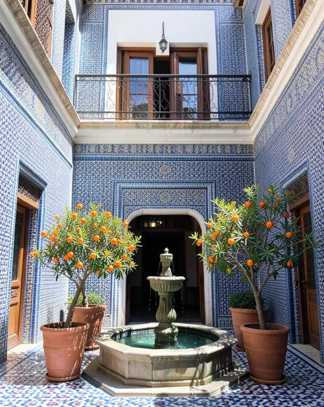 Colorful Moroccan riad courtyard with blue zellige tiles, central fountain, and orange trees