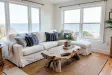 Cozy coastal cottage living room with white sofa, navy pillows, driftwood table, jute rug, and sea view