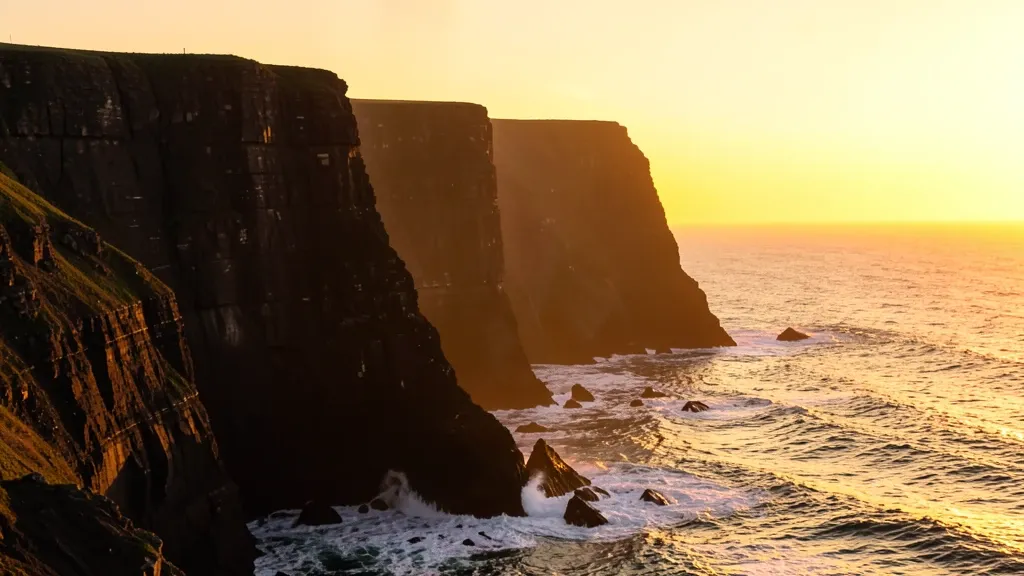 Dramatic sea cliffs at sunset with golden ocean and waves crashing against dark rocks