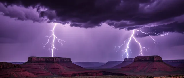 Dramatic lightning bolts behind flat-topped mesas with dark purple storm clouds and distant rain
