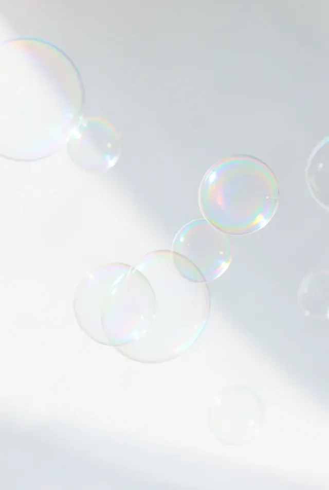 Delicate iridescent soap bubbles floating in bright window light with rainbow reflections on white