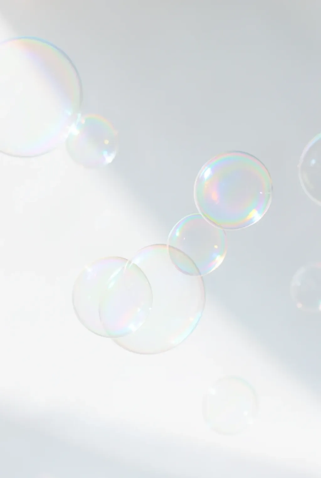 Delicate iridescent soap bubbles floating in bright window light with rainbow reflections on white