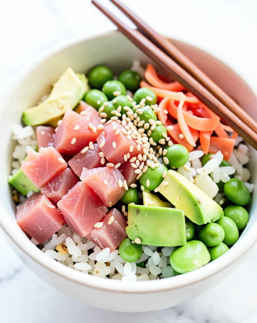 Vibrant poke bowl with tuna, sushi rice, avocado, edamame, pickled ginger, sesame seeds, and chopsticks