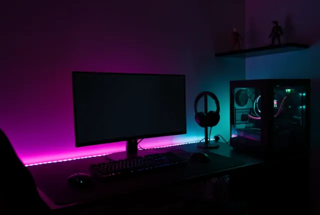 Dark bedroom gaming setup with an ultrawide monitor and a magenta to cyan RGB wall wash