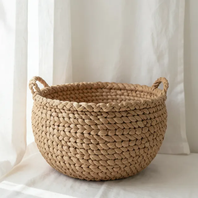 Large round handwoven seagrass basket with chunky texture against a white linen curtain