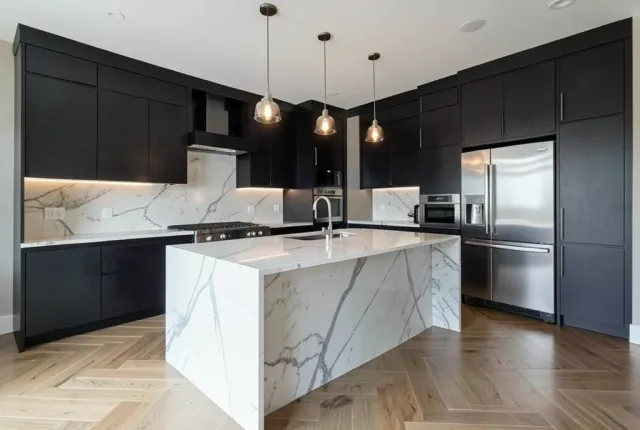 Luxury modern kitchen with marble waterfall island, pendant lights, dark cabinets, and herringbone floors