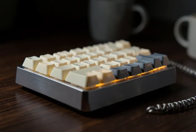 Macro of a mechanical keyboard with blank cream and grey keycaps glowing amber on a walnut desk