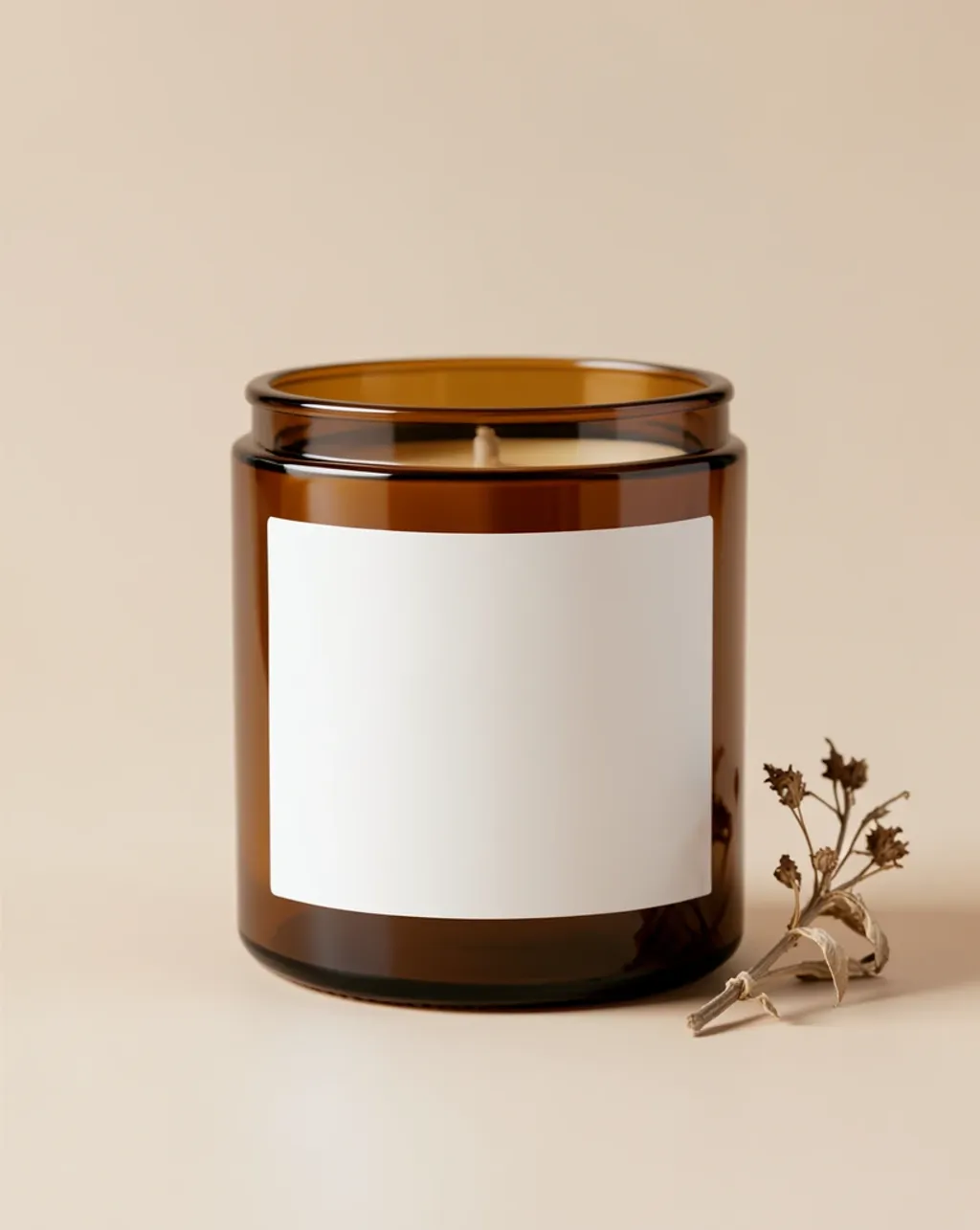 Amber glass candle jar with a blank label in soft studio light beside a small dried botanical