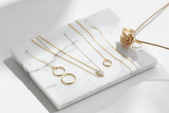 Delicate gold necklaces and rings arranged on a white marble tray with soft shadows and dried flower accent