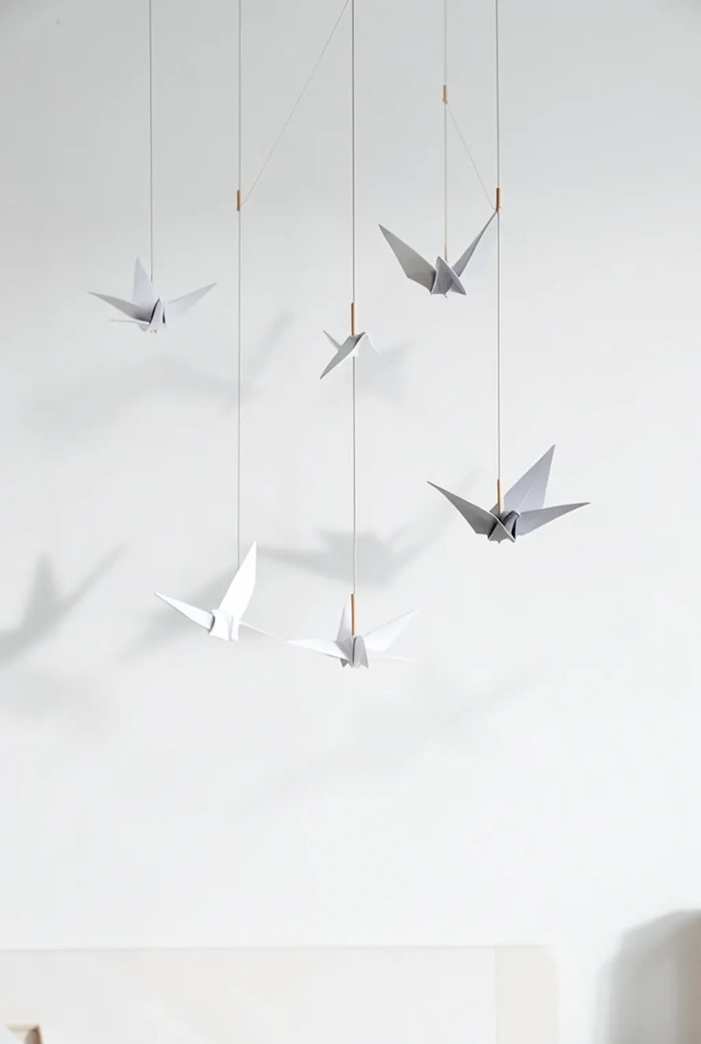 Minimalist origami crane mobile with white and grey paper cranes hanging from thin wooden rods
