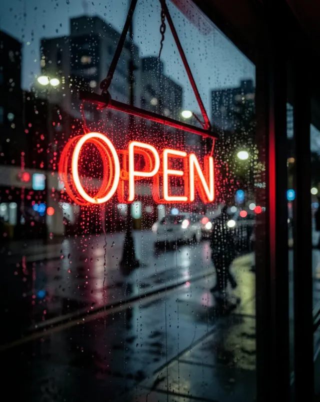 Glowing red neon open sign reflected in raindrops on a dark storefront window with blurred city lights