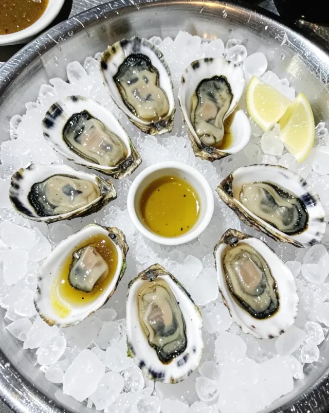 Overhead oyster bar ice bed with shucked half-shells, lemon wedges and a blank mignonette ramekin