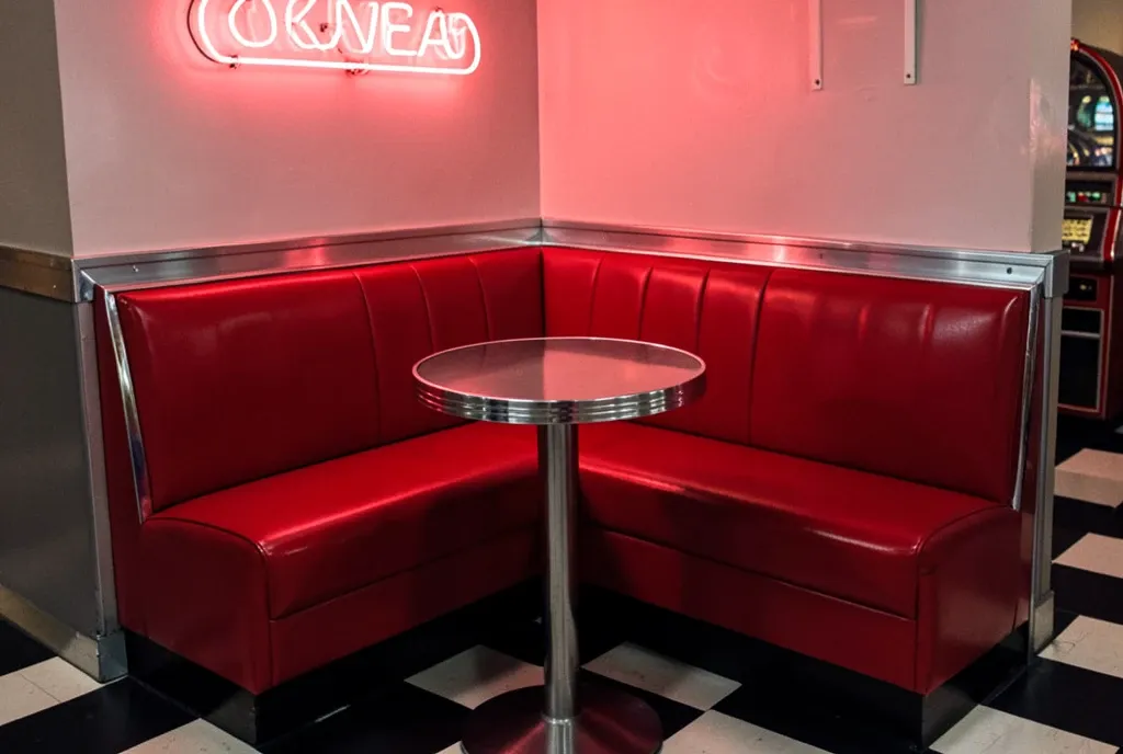 Retro red vinyl diner booth with chrome trim, checkered floor, neon glow, and jukebox in the background