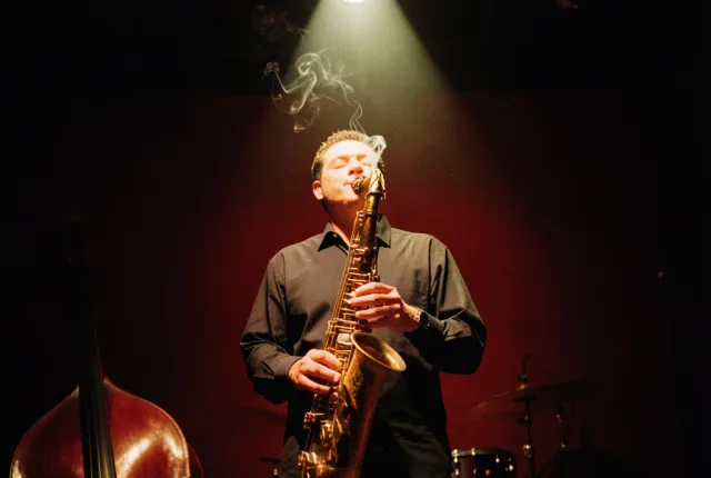 A saxophonist under a single spotlight in a dark basement jazz club, smoke in the beam.
