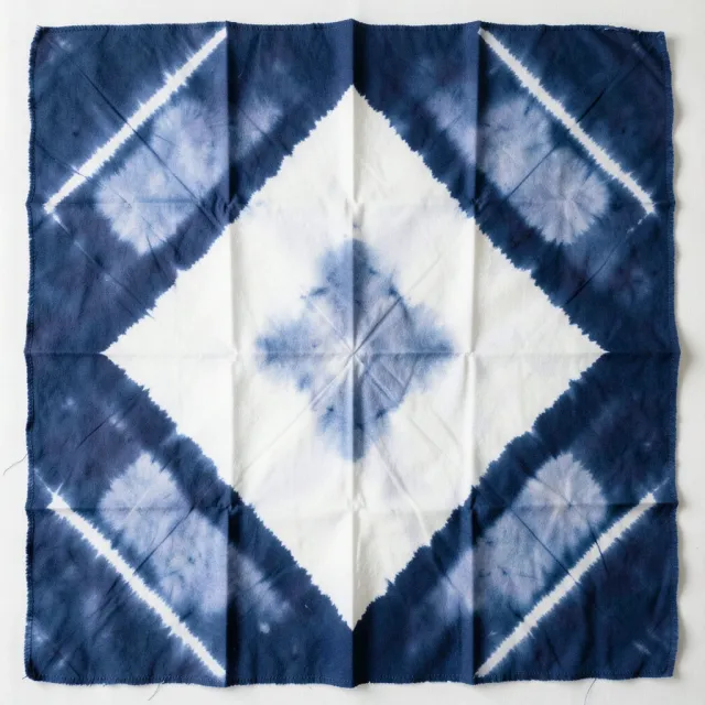Indigo shibori cloth flat-lay with white diamond clamp-resist shapes and soft dye bleed at edges