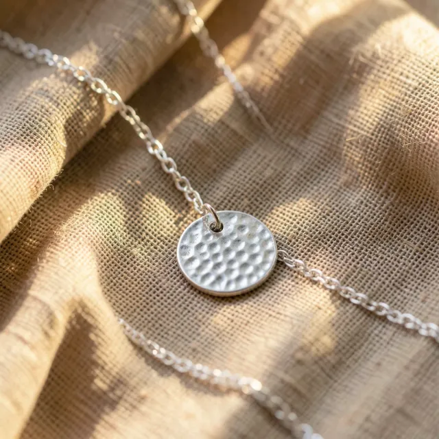 Fine silver chain with a hammered disc pendant draped in an S-curve across crumpled linen