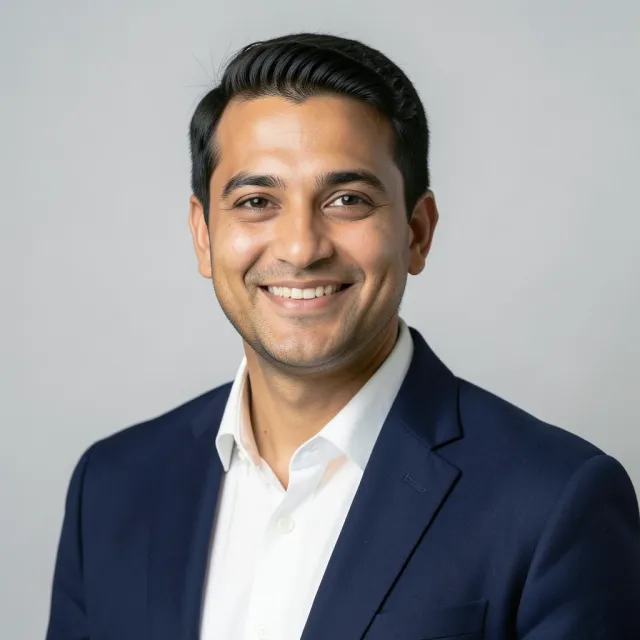 Professional studio headshot of a man in navy blazer against gray backdrop