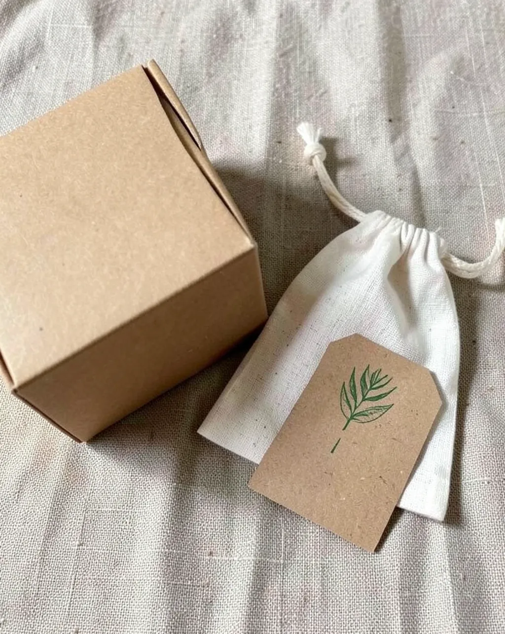 Sustainable kraft paper packaging set with cotton pouch and recycled cardboard tag on linen