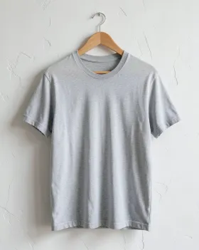 Blank heather-grey t-shirt on a wooden hanger against a plaster wall in soft natural light