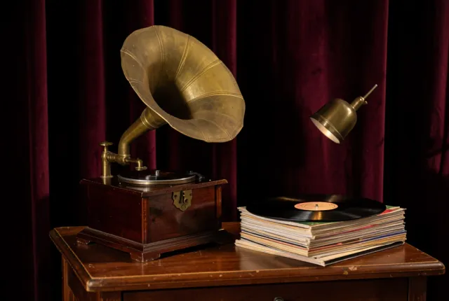 Antique brass horn gramophone beside a stack of vinyl records on a wooden side table