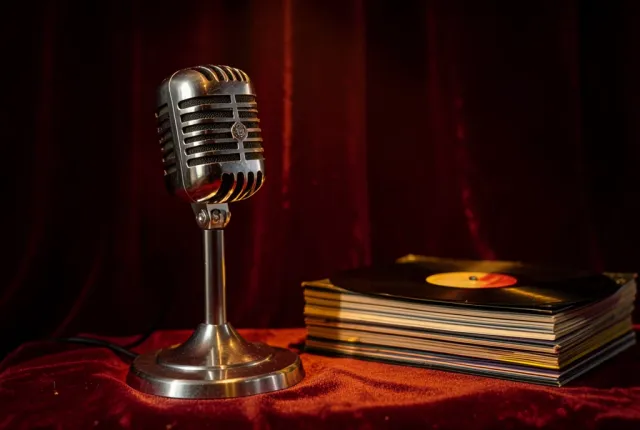 Classic chrome microphone on a stand beside a stack of vinyl records under warm spotlight